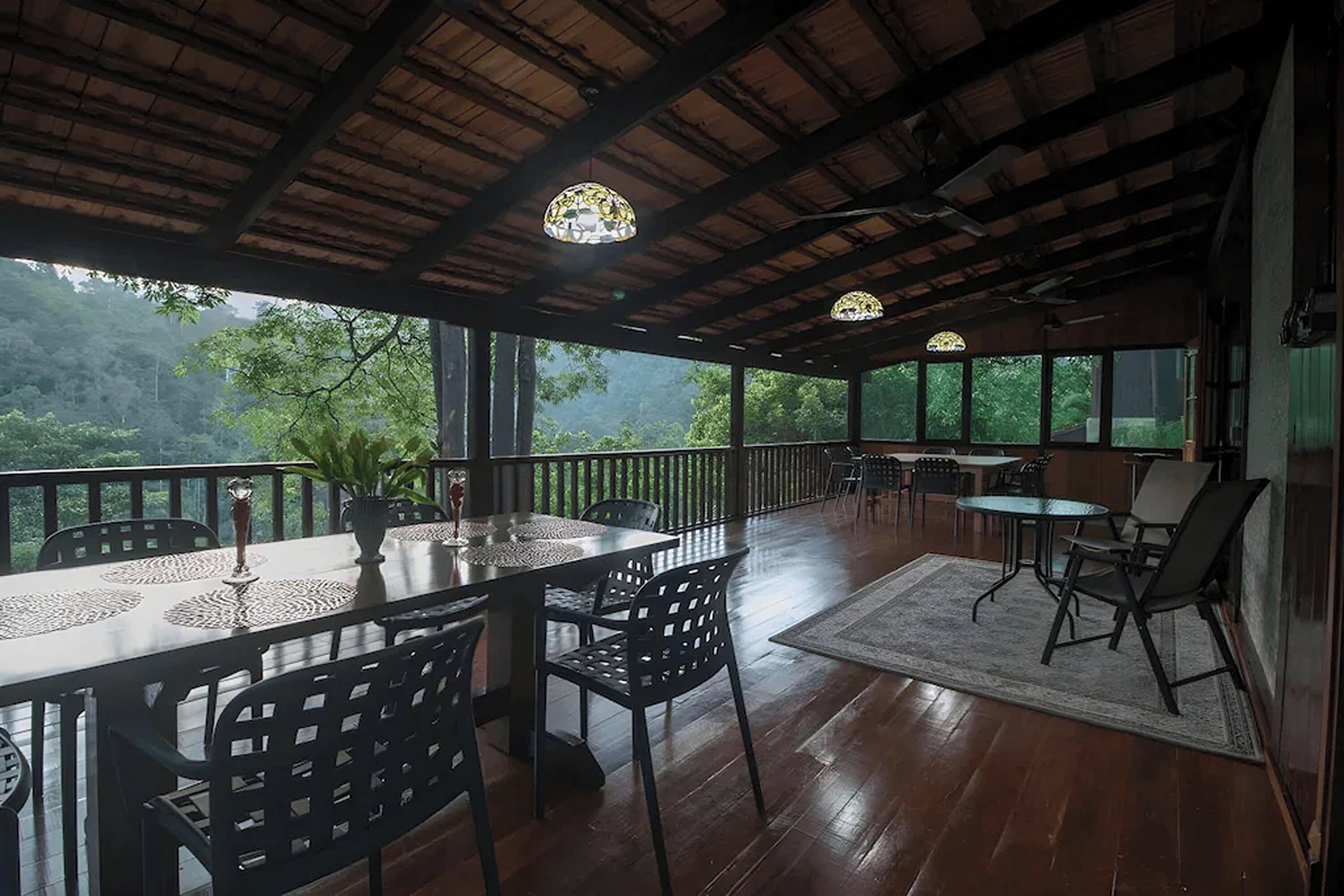 An outdoor dining area with a wooden deck, tables, chairs, and a view of the forest.