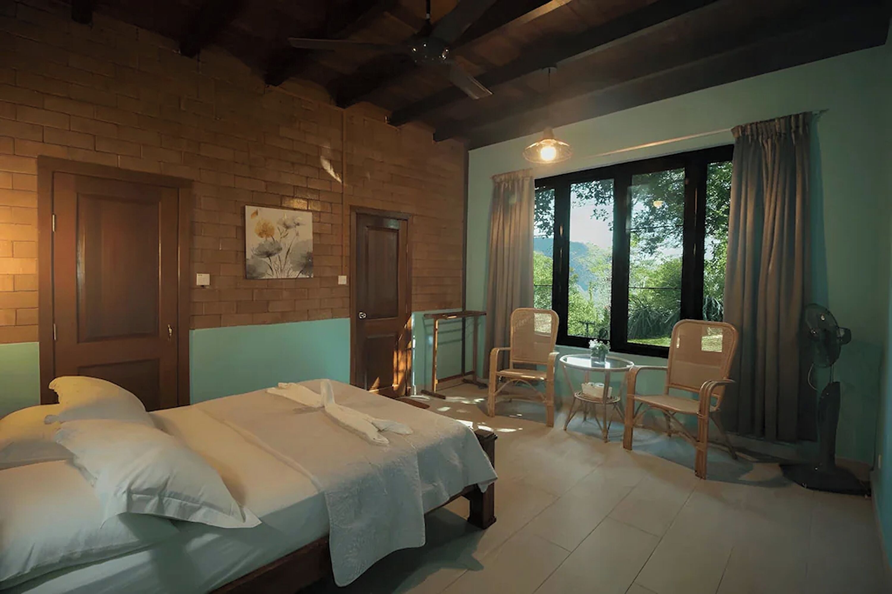 A room with two beds, a window with a view, a fan, and a table with chairs.