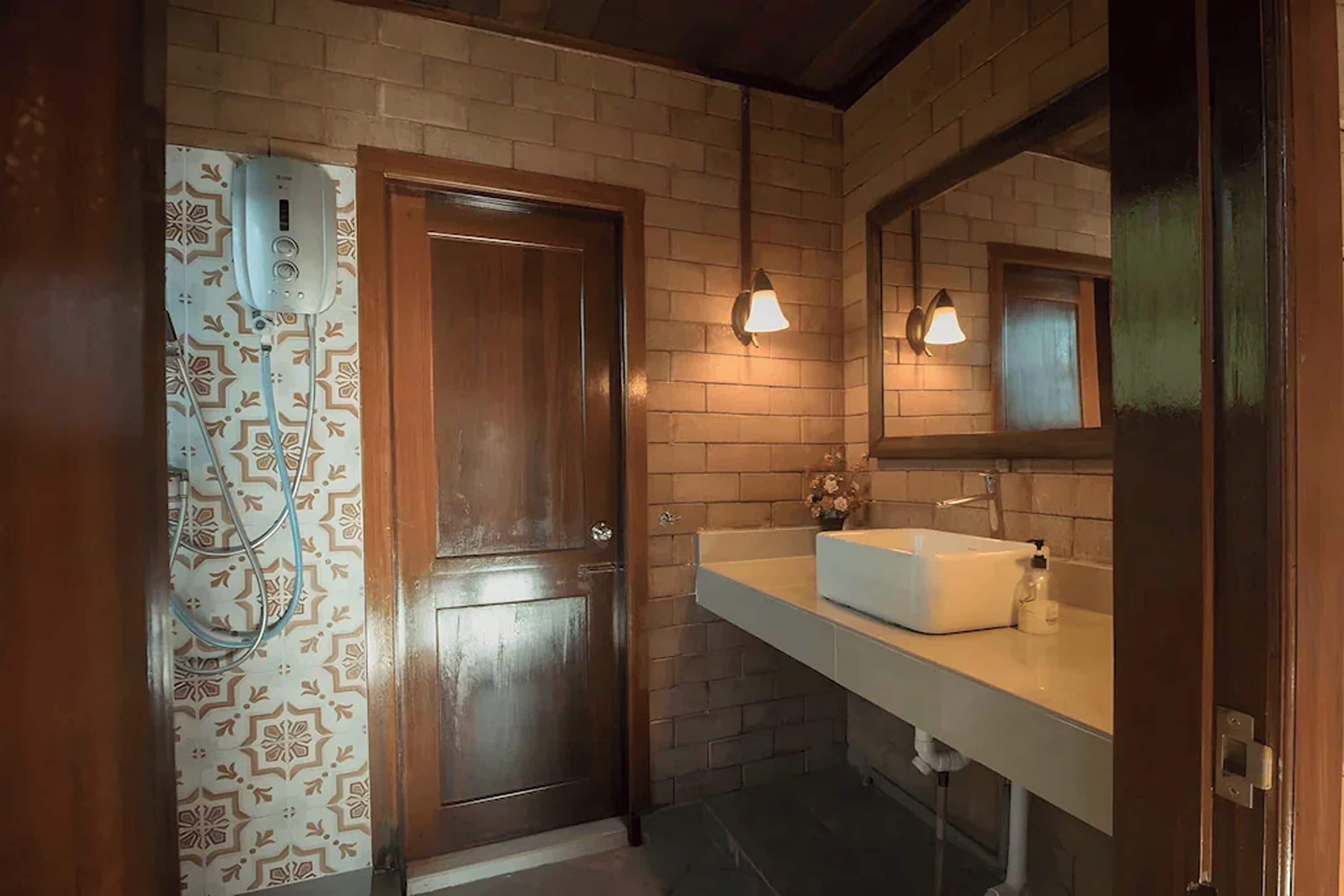 Une salle de bain avec une porte en bois, un lavabo blanc et un miroir au-dessus.