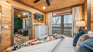 A wooden-paneled bedroom with a bed, a TV, and a window with curtains. - New - Dollywood - Fire pit - Arcade - Family Getaway (Sevierville)