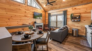 A cozy cabin interior with a dining area, a fireplace, a sofa, and a kitchen. - New - Dollywood - Fire pit - Arcade - Family Getaway (Sevierville)