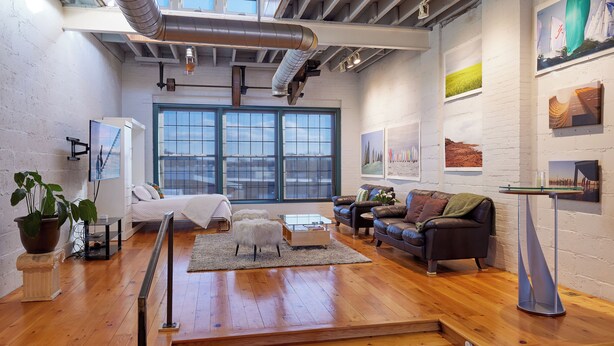 A modern living room with a bed, sofas, a coffee table, and artwork on the walls. - Luxury Loft in the Rochester Public Market! (Rochester)