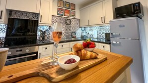 Een keuken met witte kastjes, een magnetron, een koelkast en een houten aanrecht met een glas wijn, aardbeien en een croissant.