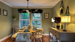 Een eetruimte met een houten tafel gedekt voor vier personen, omringd door stoelen. Er is een raam met uitzicht op groen.