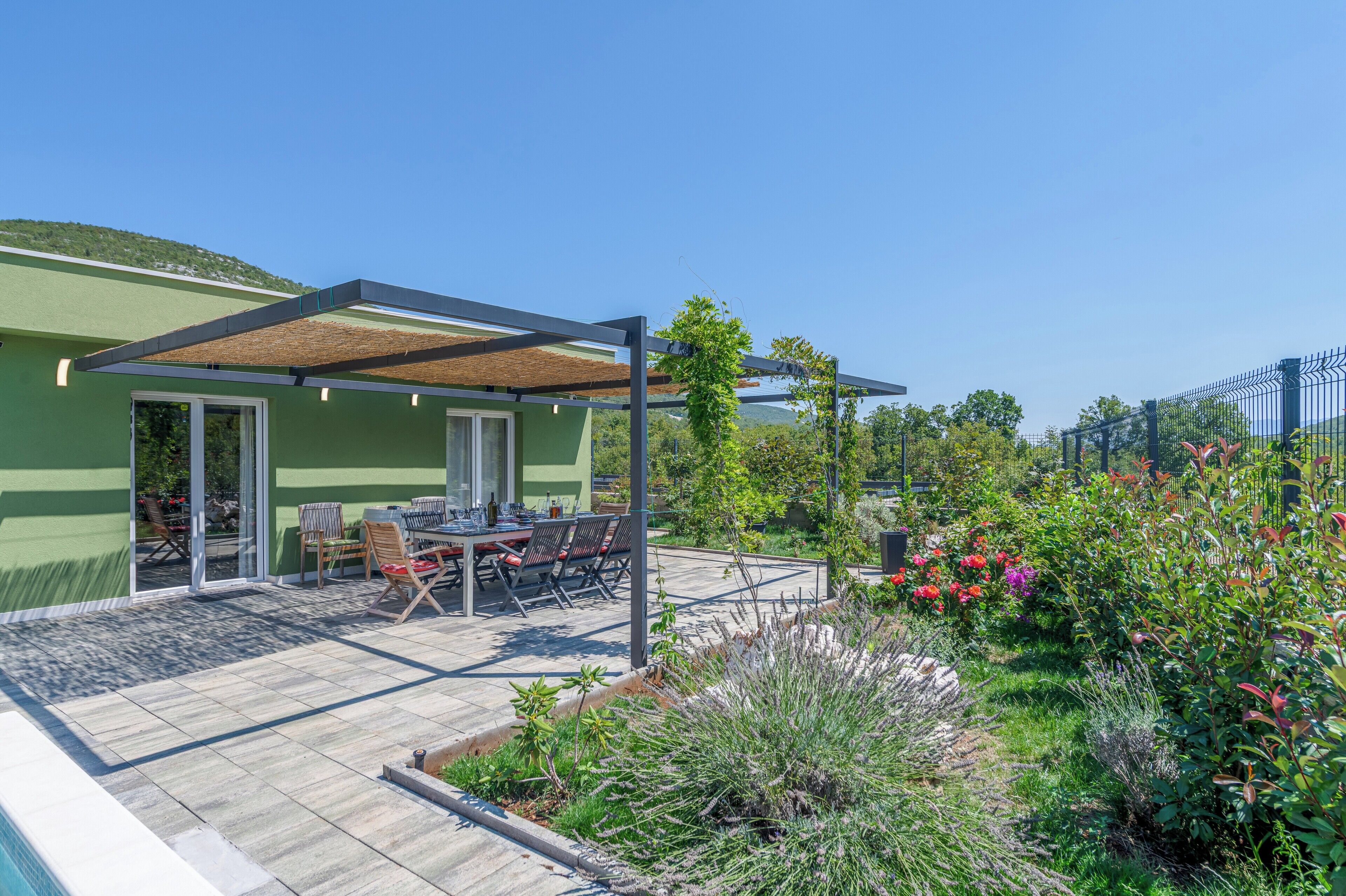 A patio area with a table and chairs, a pergola, and a garden with various plants and flowers.