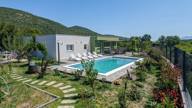 A residential property with a swimming pool, a patio area with lounge chairs, and a garden with a stone pathway.