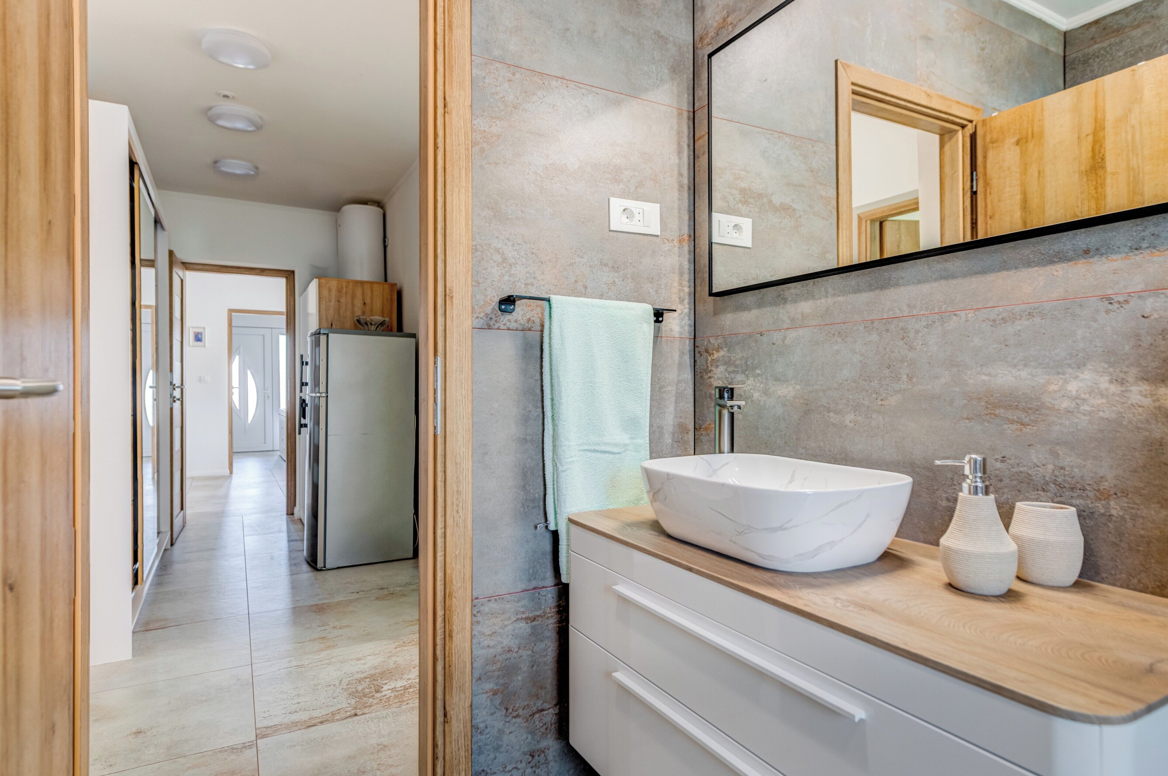 A modern bathroom with a large mirror, a white vessel sink, and a wooden vanity.