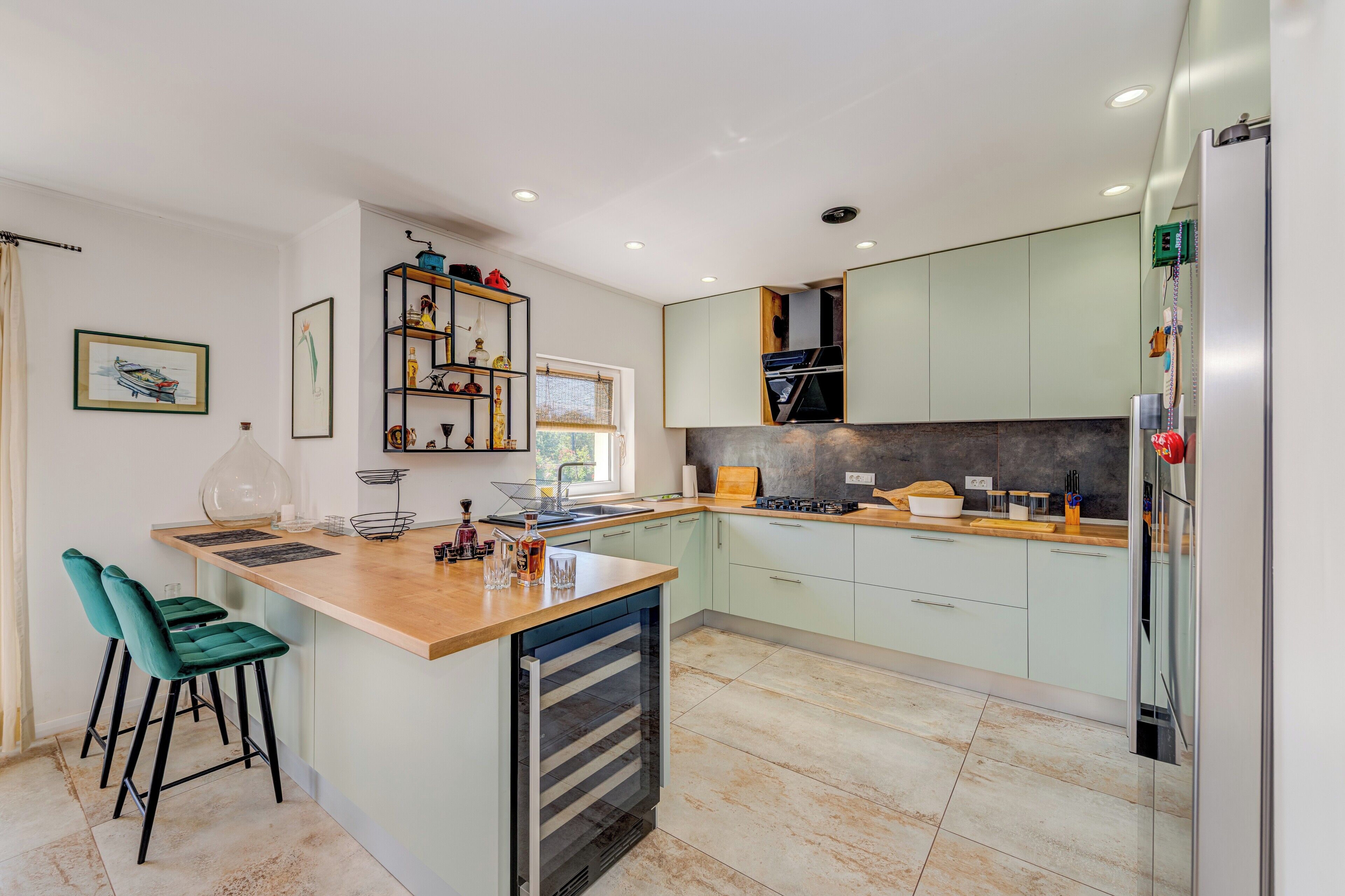 Une cuisine moderne dotée d’un îlot central, de meubles de couleur vert clair et d’un four encastré.