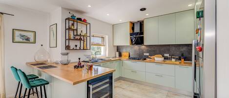 Une cuisine moderne dotée d’un îlot central, de meubles de couleur vert clair et d’un four encastré.