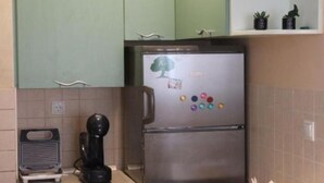 Une cuisine avec des meubles de couleur verte, un réfrigérateur en acier inoxydable, une machine à café et une horloge posée sur une étagère.