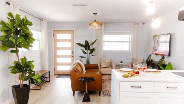 A modern living room with a brown sofa, a coffee table, and a dining area with a white table set for two.