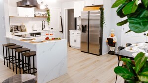 A modern kitchen with white cabinets, a large island with bar stools, a stainless steel refrigerator, and a dining area with a table set for two.