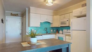 Une cuisine avec des meubles blancs, un pare-feu turquoise et un plan de travail en bois.