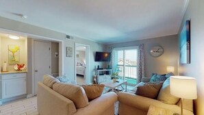 Un salon avec des canapés de couleur beige, une table basse et un téléviseur. Il y a un balcon avec vue.
