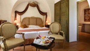 Ein Hotelzimmer mit einem großen Bett, zwei Sesseln, einem Tablett mit Frühstück und einem klassischen Rundbogenportal.