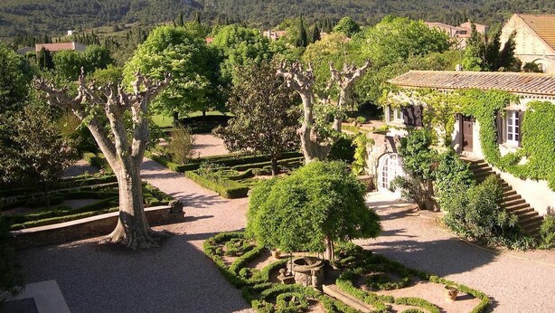 Ein angelegter Garten mit Wegen, Bäumen und einem Gebäude mit Ziegeldach.