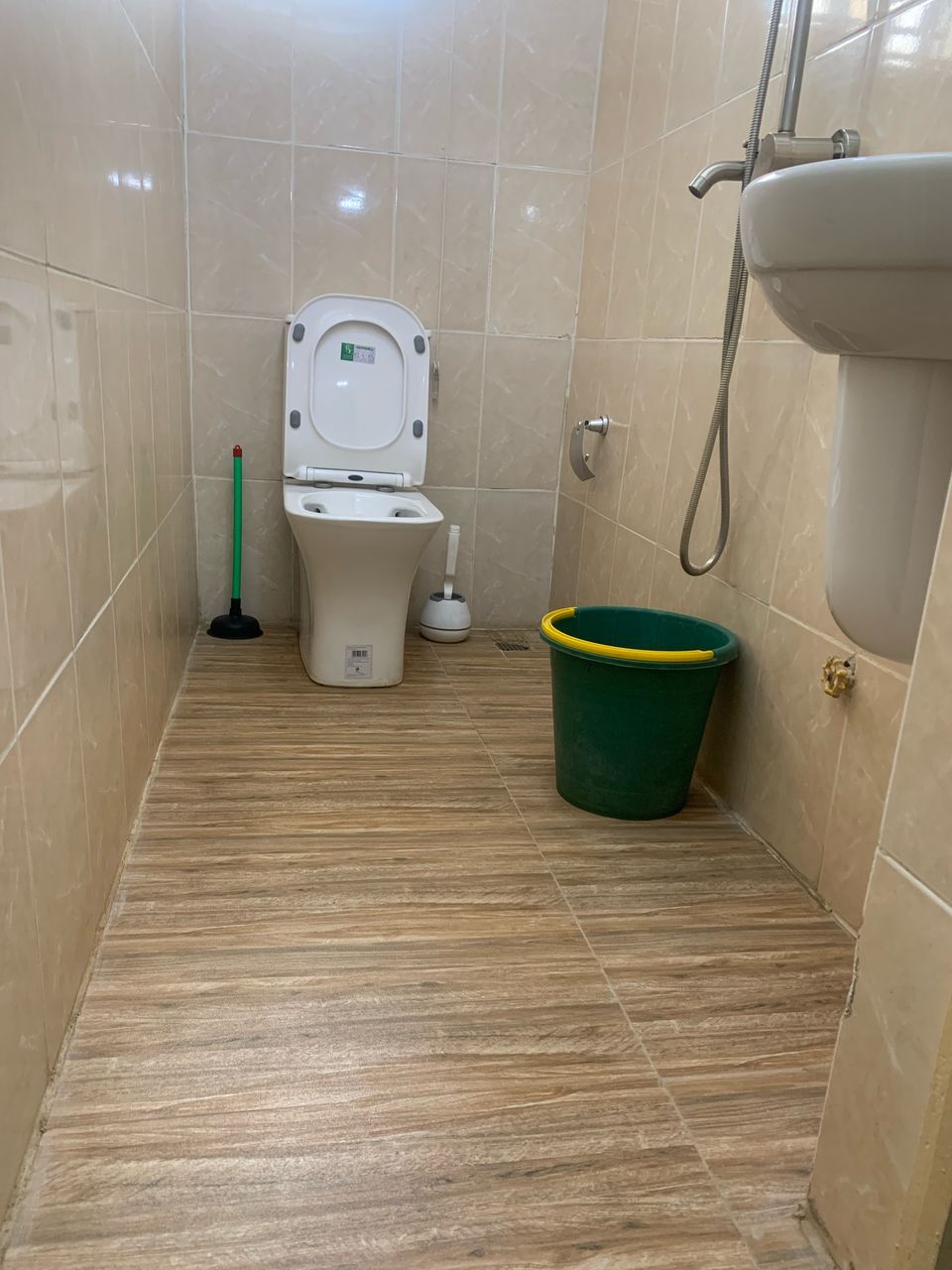 Un baño pequeño con un inodoro, un balde verde y una ducha.