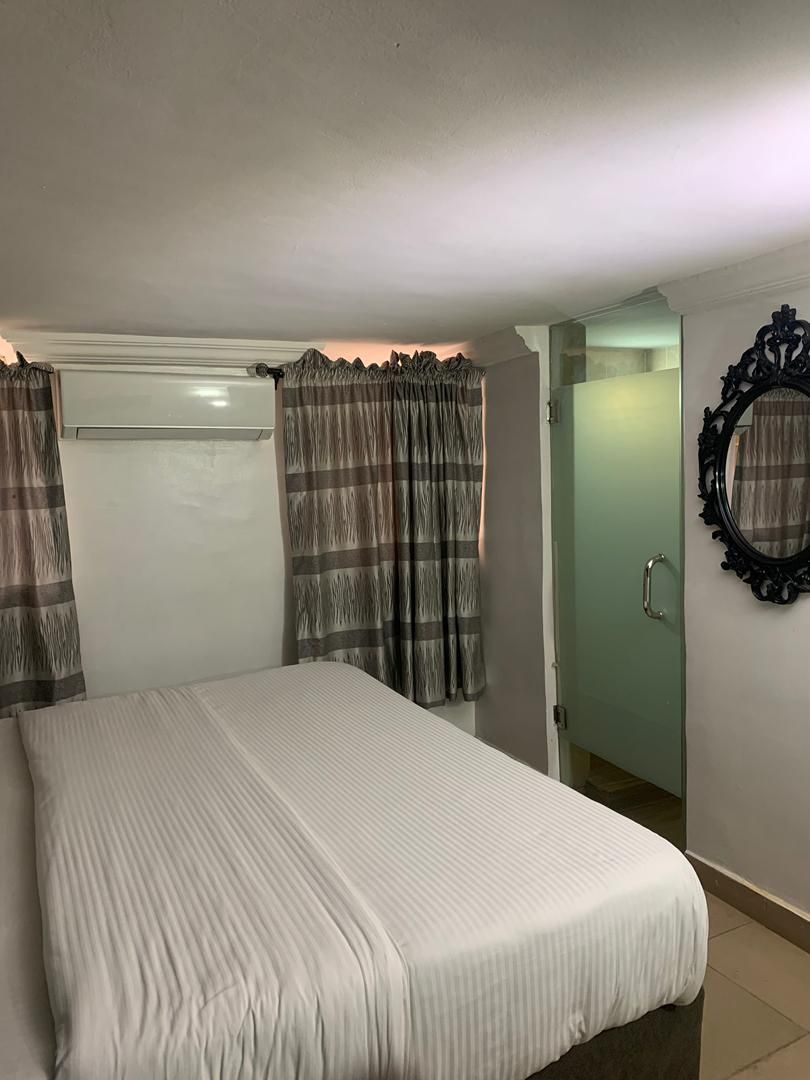 A bedroom with a bed, curtains, a wardrobe, and a mirror.