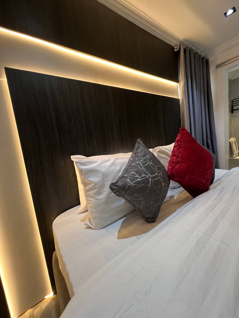 Une chambre d’hôtel avec une tête de lit en bois foncé, une couvre-lit blanche et deux oreillers, dont l’un est à motifs de marbre et l’autre est rouge.