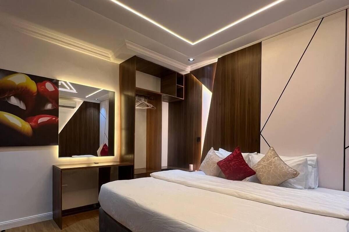 A modern bedroom with a large bed, built-in wardrobe, and a wall-mounted TV.