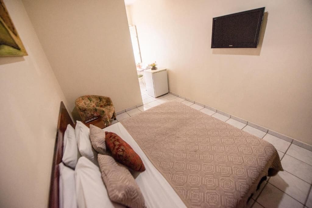 Una habitación pequeña y limpia con cama, una silla, televisión y una mesita con una planta.