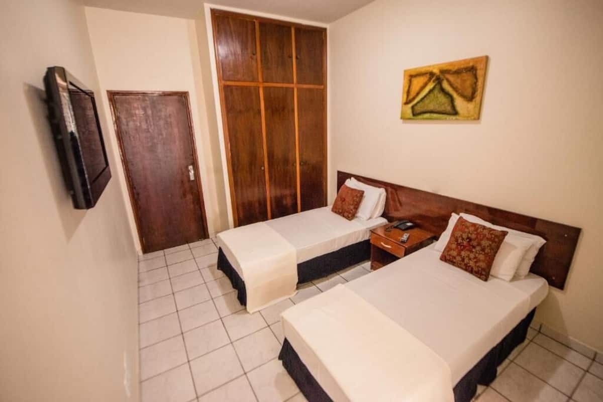 A hotel room with two beds, a wardrobe, a television, and a painting on the wall.