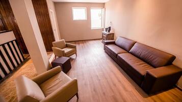 A spacious living room with a brown leather sofa, beige armchairs, and a wooden floor.