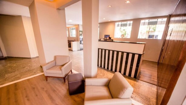 A spacious lobby with a wooden floor, a reception desk, and two white armchairs. - Havana Economy (Uberaba)