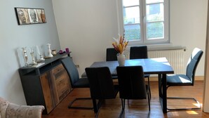 En matplats med ett träbord, svarta stolar, en vit vas med blommor och ett svart skåp med dekorativa föremål.
