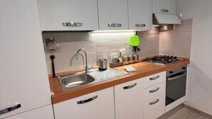Ett modernt kök med vita skåp, en diskho i rostfritt stål, en gasspis och en inbyggd ugn.