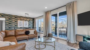 A modern living room with a leather sofa, a glass coffee table, and a large window with a balcony. - Fast WiFi | Prof Cleaned | Linen & Towels | Coffee (Seaside Heights)