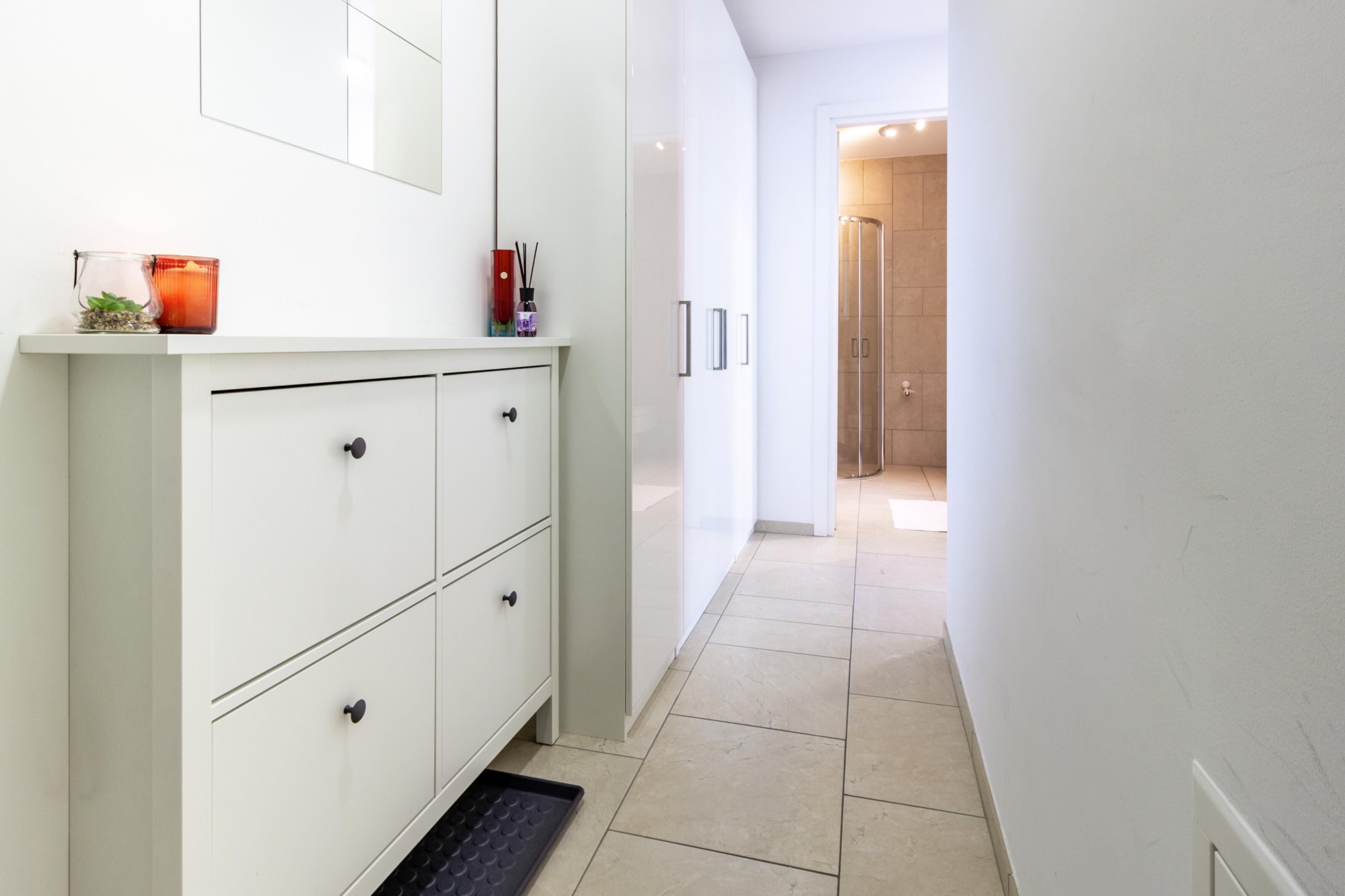 Un couloir étroit avec une armoire blanche, une petite plante et une bougie rouge sur le côté gauche.