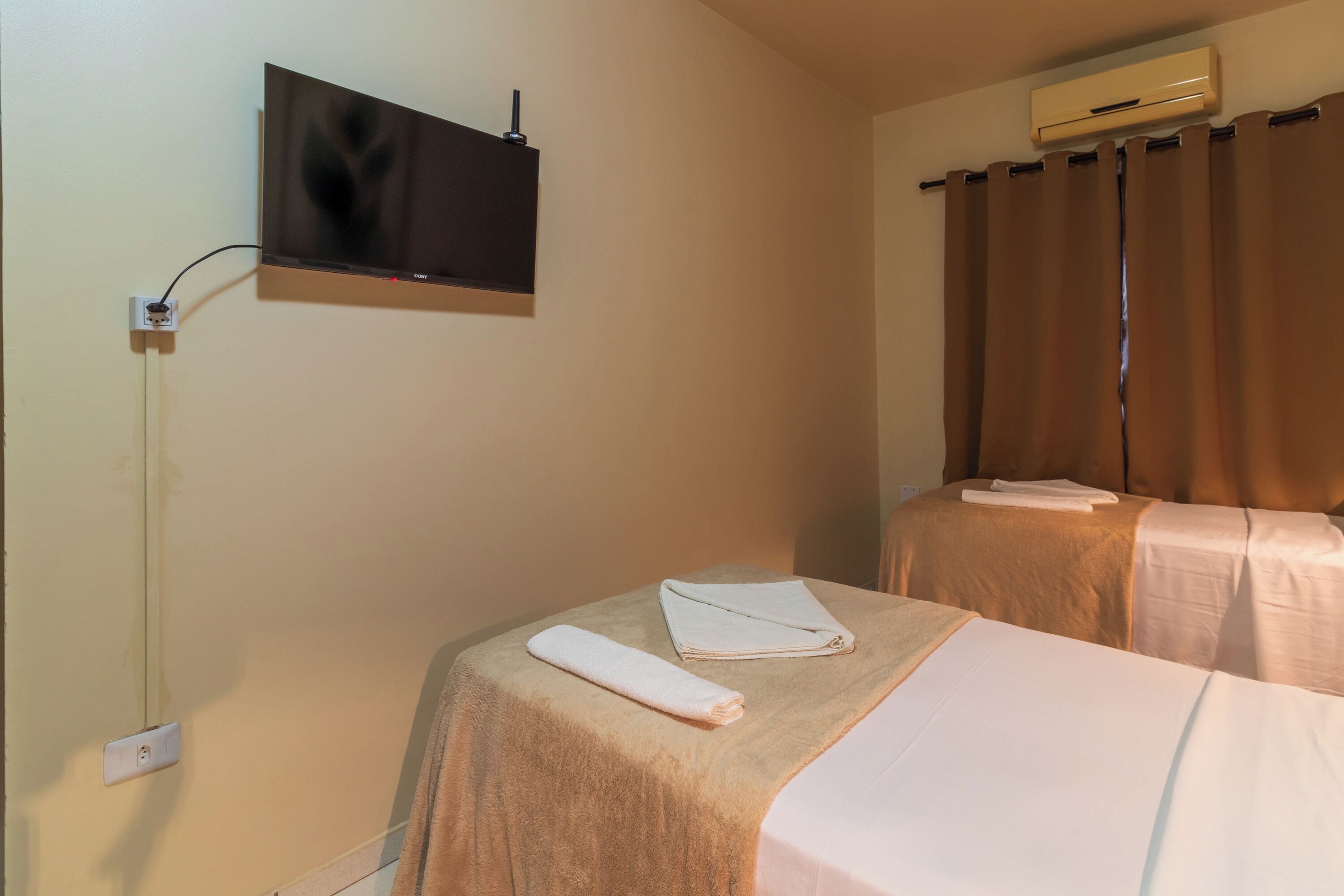 Habitación de hotel con dos camas, un televisor montado en la pared, aire acondicionado y un enchufe.