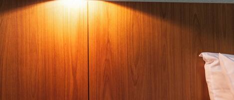 Cabecera de madera con una lámpara de pared, una mesita de noche con un control remoto y una cama con ropa de cama blanca.