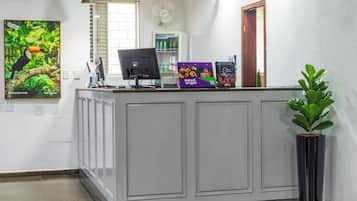 Balcão de recepção com computador, ventilador e planta em vaso.