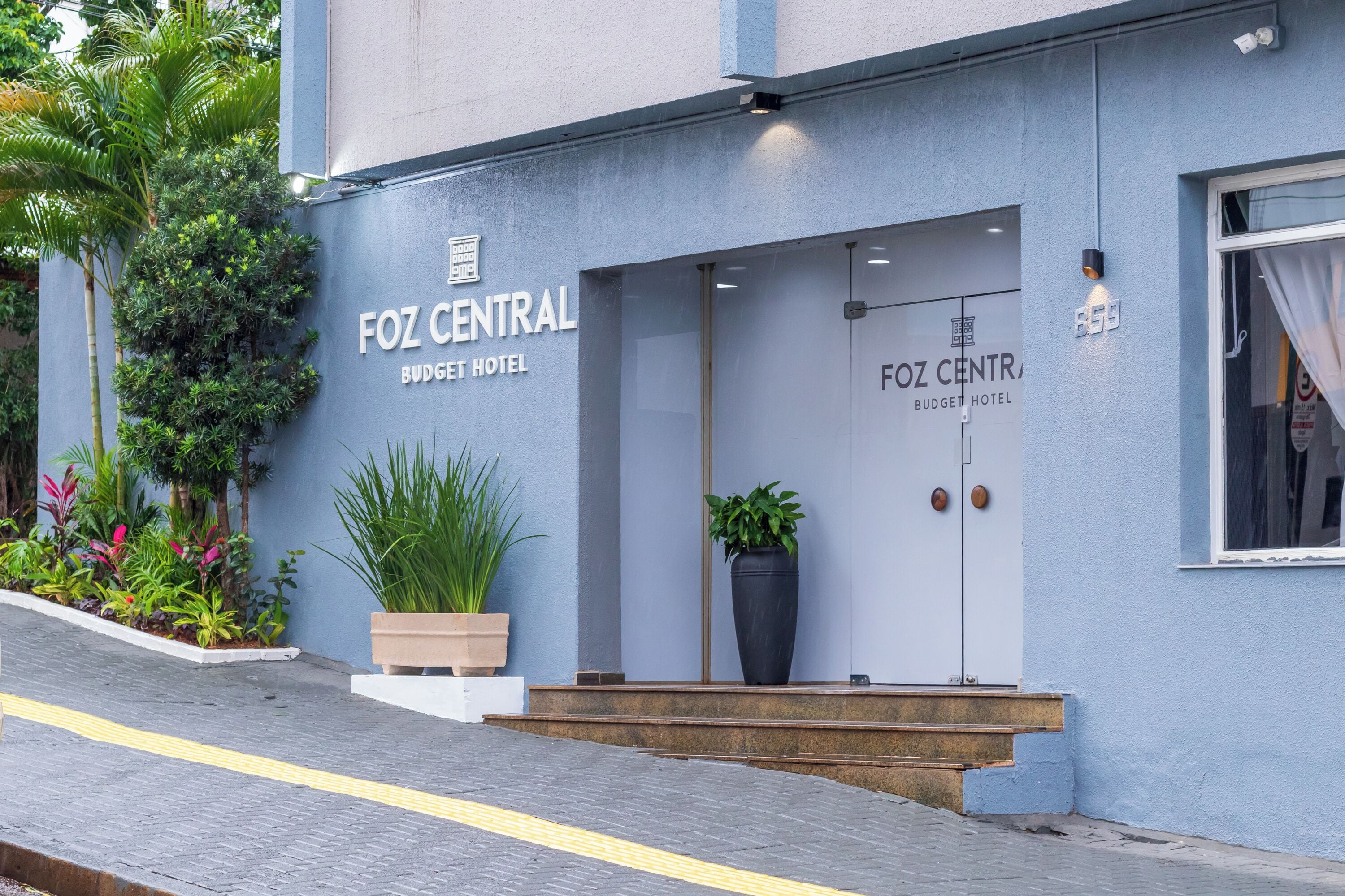 Exterior do Hotel Foz Central Budget, com fachada moderna, ampla entrada e plantas em vasos.