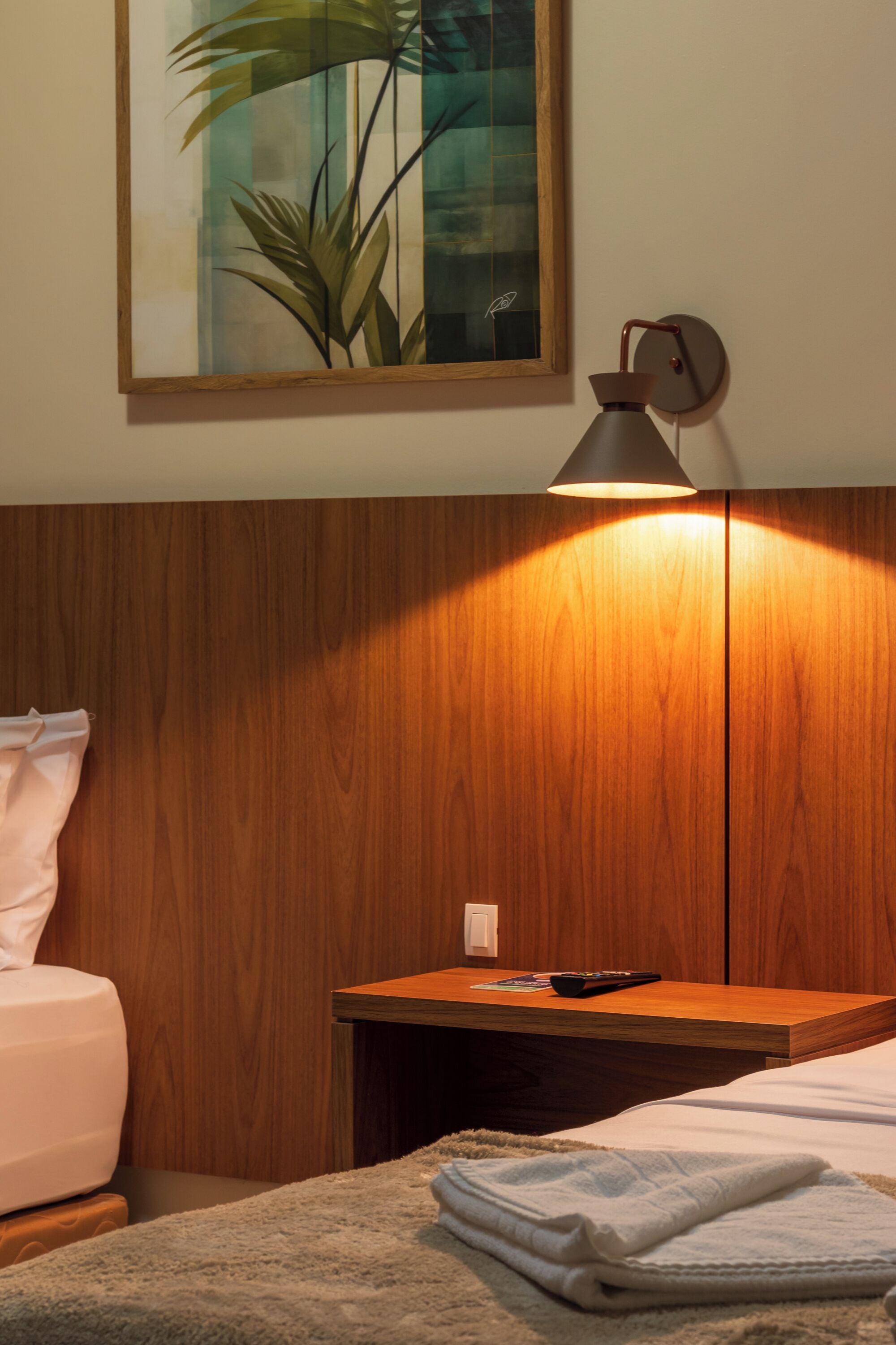 Une chambre avec une tête de lit en bois, une table de chevet avec une lampe, un lit avec une couverture et un tableau accroché au mur.