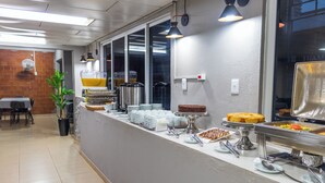 A buffet setup with various food items and utensils. - Foz Central Budget Hotel (Foz do Iguacu)