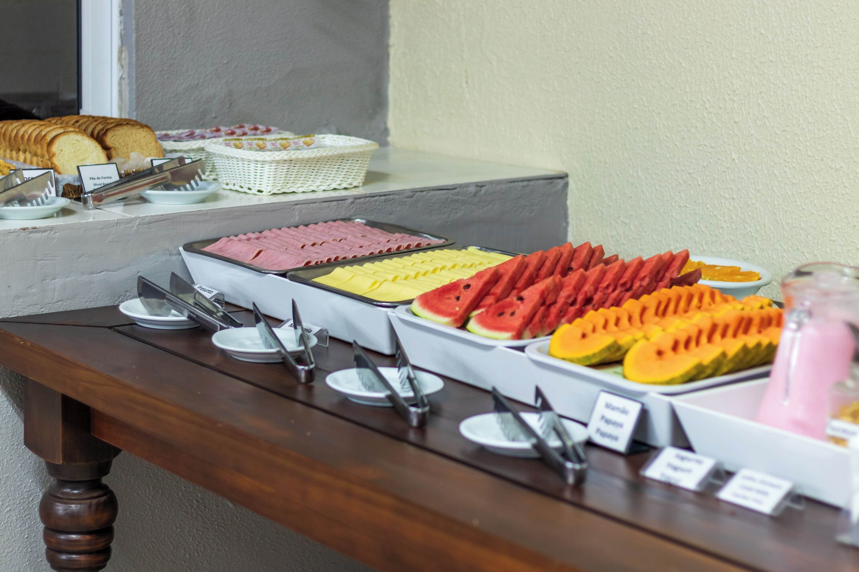 Une table de buffet proposant divers aliments, notamment des tranches de pain, du jambon, du fromage, de la pastèque et de la papaye.