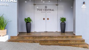 The entrance to the Foz Central Budget Hotel with a clear glass door, two potted plants on either side, and a sign above the door. - Foz Central Budget Hotel (Foz do Iguacu)