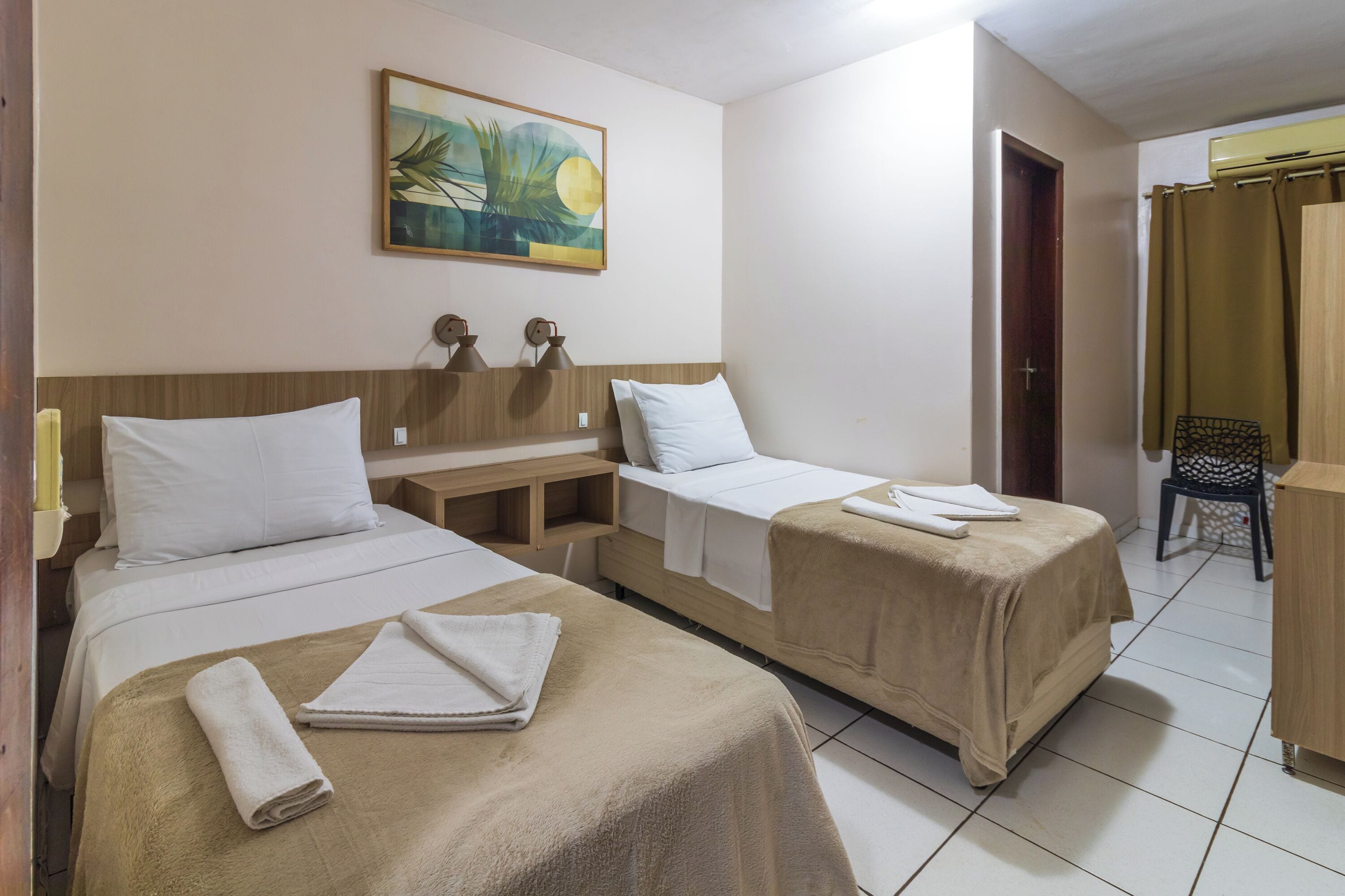 A hotel room with two single beds, a wooden headboard, a painting, a desk, and a chair.