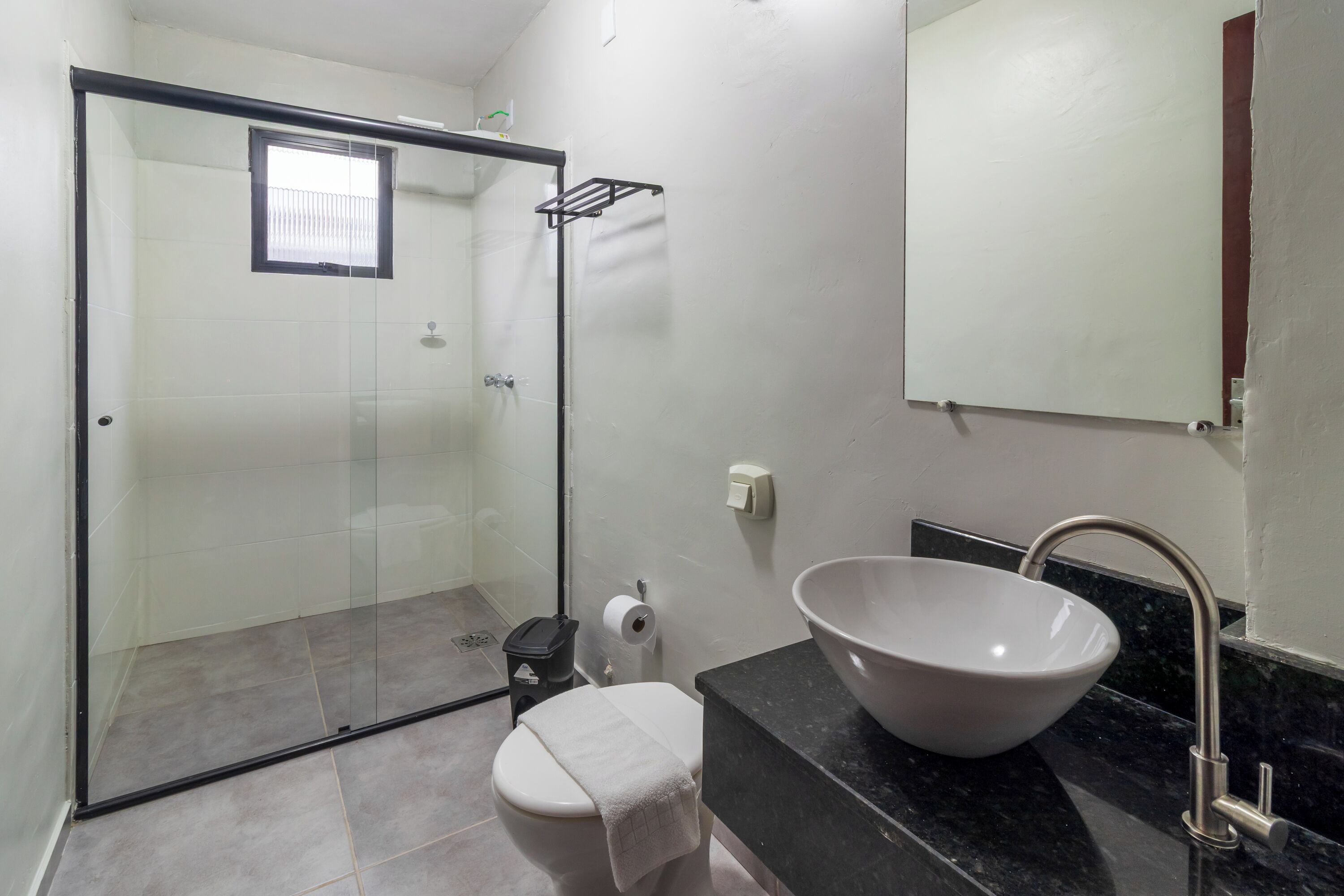 Un baño con cabina de ducha de vidrio, inodoro, lavabo con recipiente amplio y espejo sobre el lavabo.