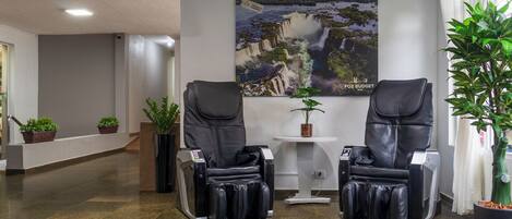 Een wellnessruimte met twee massagestoelen, een poster aan de muur en potplanten.