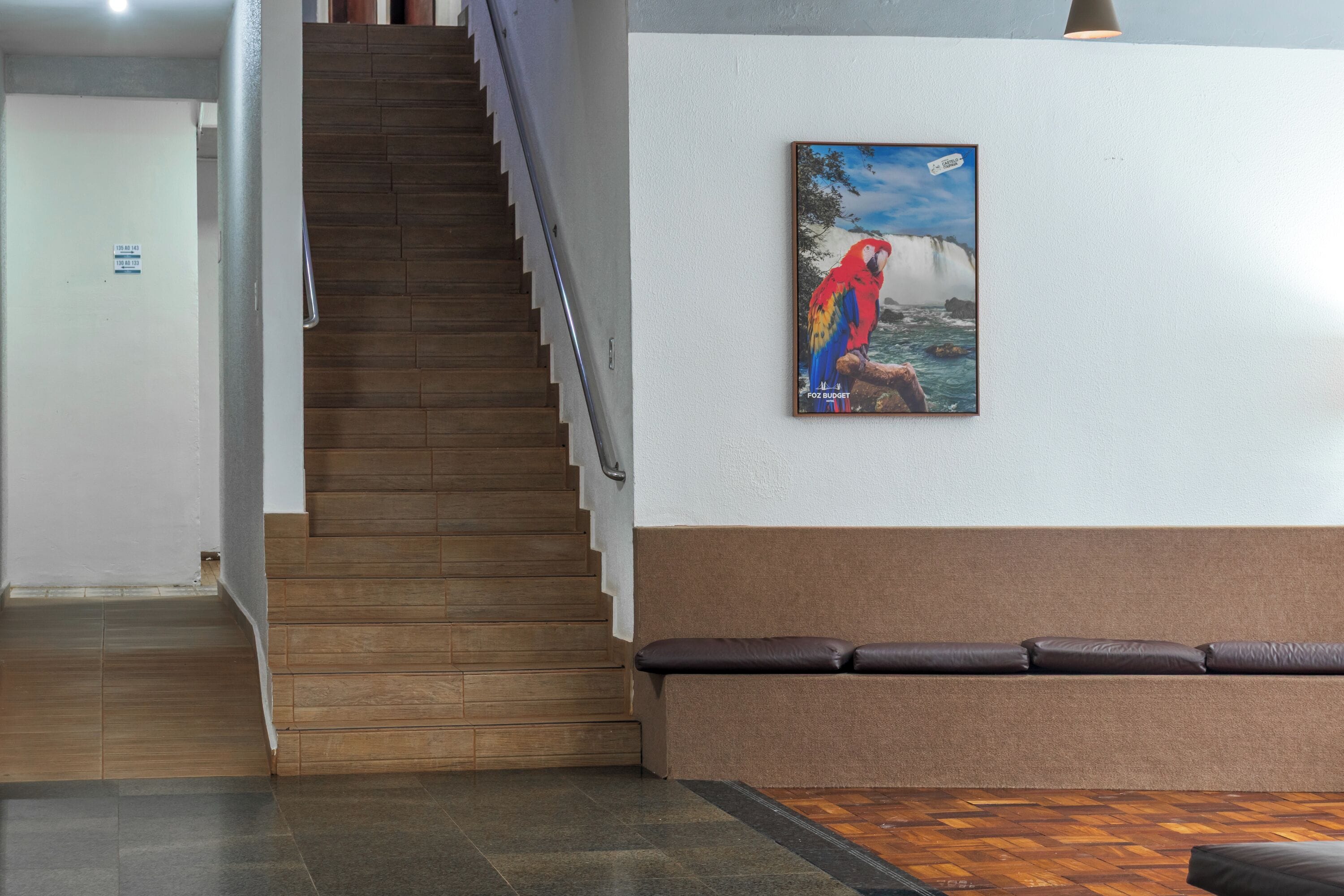 Un escalier menant à un palier où se trouve un banc rembourré et un tableau encadré représentant un perroquet.