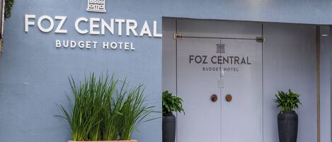 Foz Central Budget -hotellin ulkopuoli: moderni julkisivu, suuri sisäänkäyntiovi ja kaksi ruukussa olevaa kasvia molemmin puolin ovea.
