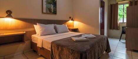 Una habitación de hotel con cama, mesitas de noche, un cuadro y una ventana con cortinas.