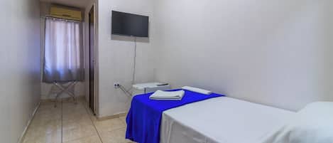 Una stanza piccola e pulita con un letto, una TV a parete e un bagno con tenda doccia.
