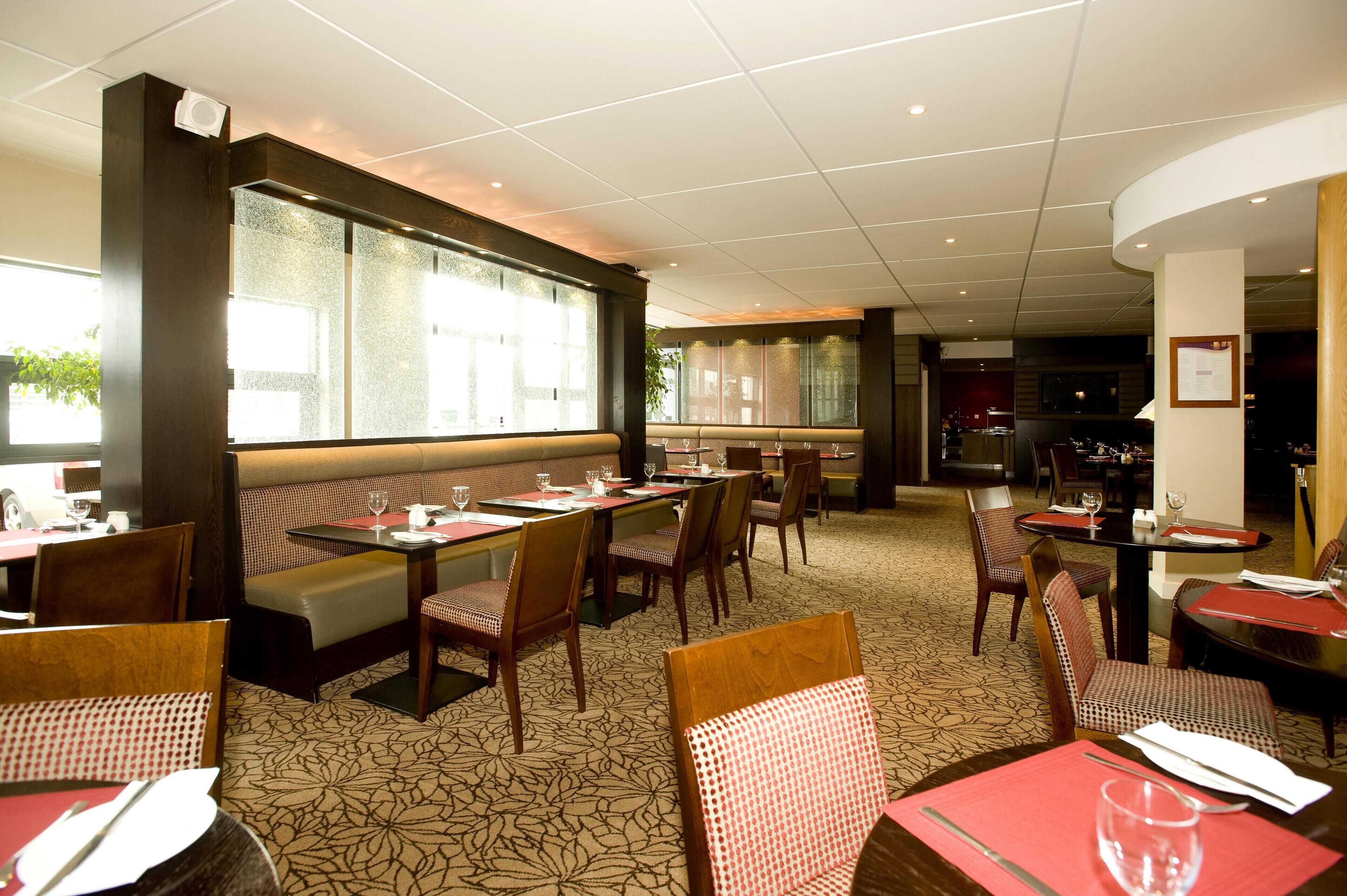A restaurant with booths, tables, and chairs, featuring a patterned carpet and a large window.
