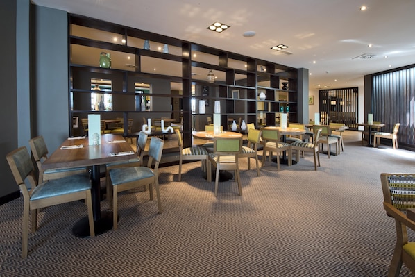 Un hall d’hôtel doté d’un espace salon central, de plusieurs tables et d’un mur décoratif agrémenté d’étagères.