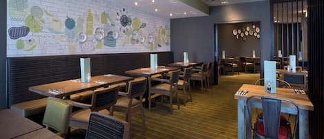 Een restaurant met houten tafels en stoelen, een muurschildering van baksteen en een kamerbreed tapijt met patroon.
